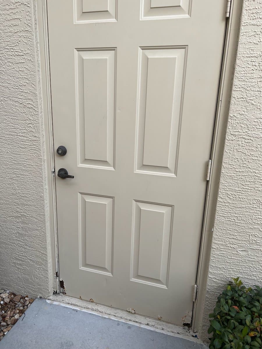 Old beige exterior door with worn bottom edge and weathering