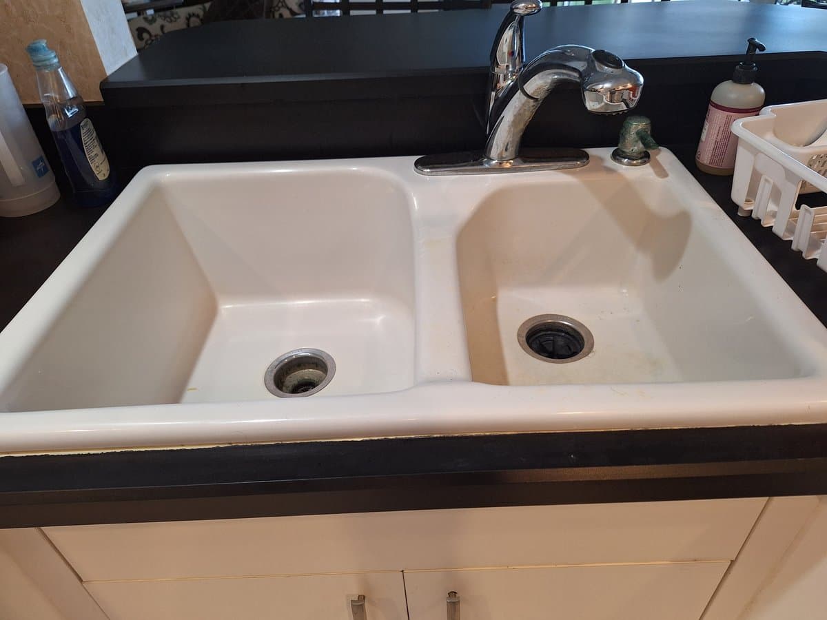 Old white porcelain double-bowl kitchen sink with basic faucet